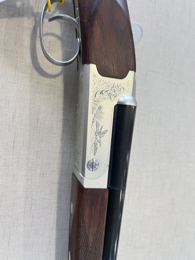 Parte de espingarda com madeira escura e metal gravado em fundo cinza