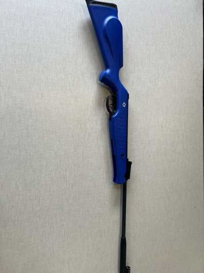 Arma de pressão azul com cano preto encostada numa parede clara