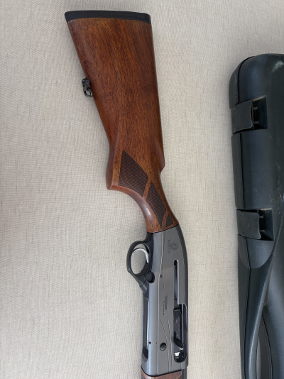 Espingarda semiautomática Beretta com coronha em madeira e metal cinza ao lado de estojo preto.