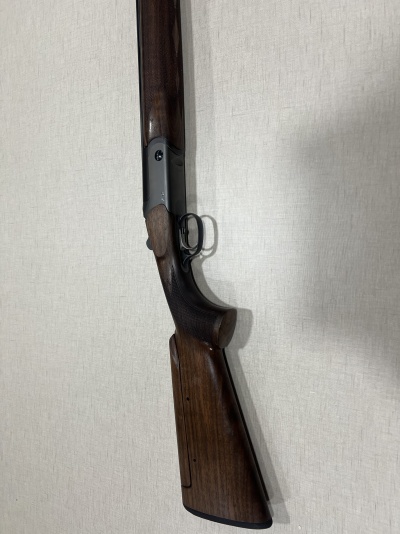 Espingarda com coronha de madeira escura e acabamento polido encostada em parede branca