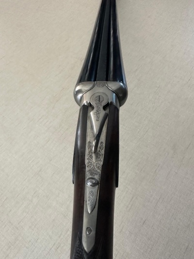 Espingarda de canos paralelos em metal preto e madeira escura com entalhes e detalhes metálicos gravados.