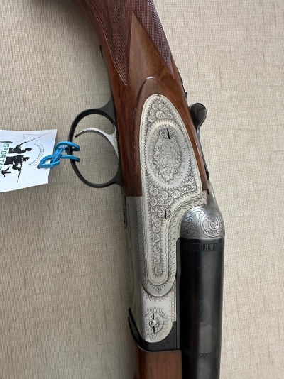 Espingarda de cano duplo com estrutura gravada e madeira castanha em fundo bege