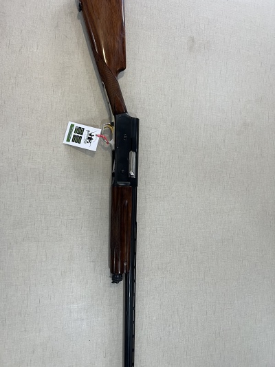 Espingarda de caça com madeira castanha e metal preto, etiqueta pendurada e fundo claro