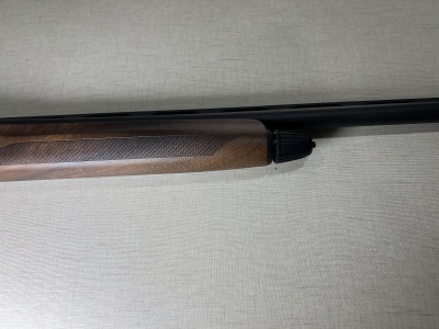 Espingarda com madeira e cano preto sobre fundo bege.