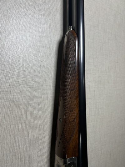 Espingarda com coronha em madeira e cano preto encostada a parede.