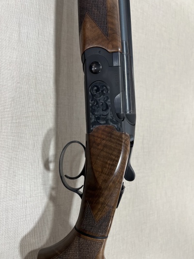 Arma de caça com madeira castanha e detalhes em preto encostada na parede