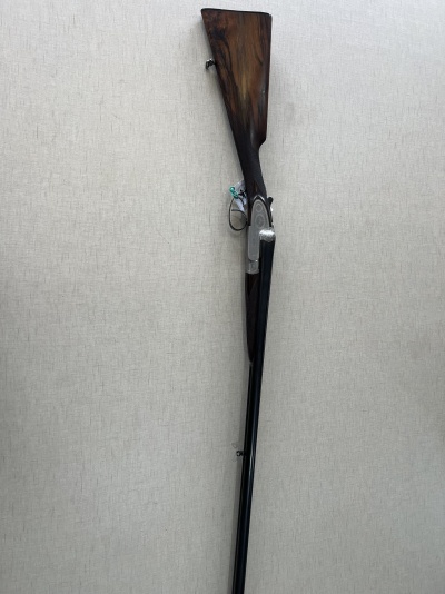 Espingarda com coronha de madeira e canos paralelos encostada a uma parede clara