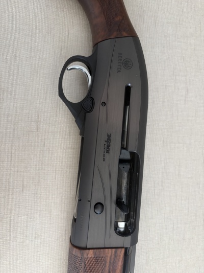 Espingarda Beretta com empunhadura em madeira e corpo preto com texto BERETTA e XPLOR unico sobre fundo bege.