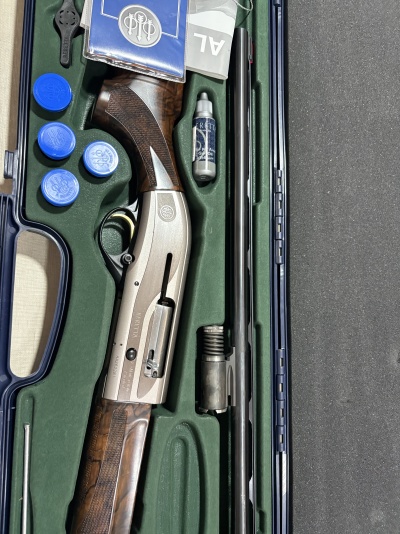 Estojo azul com espingarda Beretta, cápsulas azuis, óleo para armas e manuais.