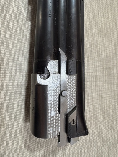 Parte daço de arma de fogo em metal preto e prateado sobre tecido bege.