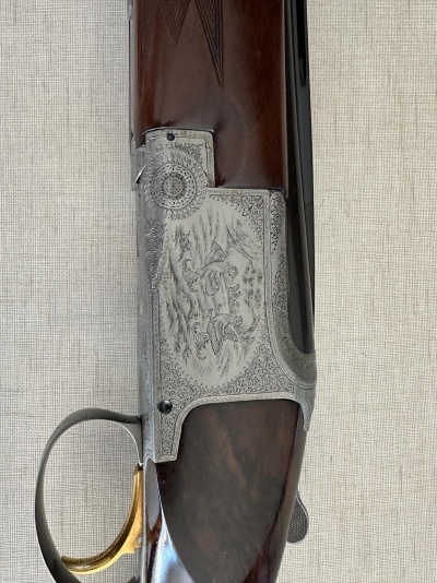 Arma de caça com punho em madeira castanha, corpo metálico gravado e gatilho dourado