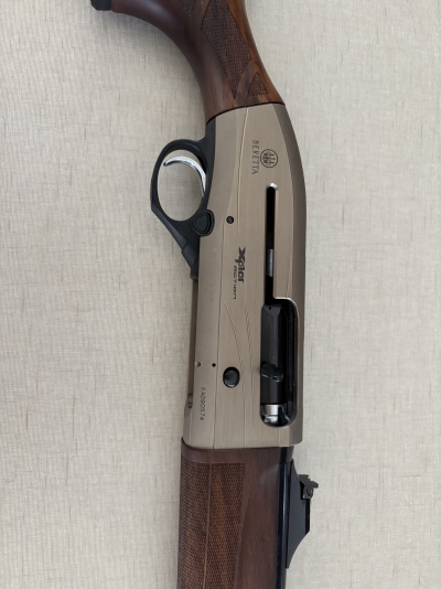 Espingarda Beretta em metal cinzento e madeira castanha com gatilho prateado sobre fundo bege