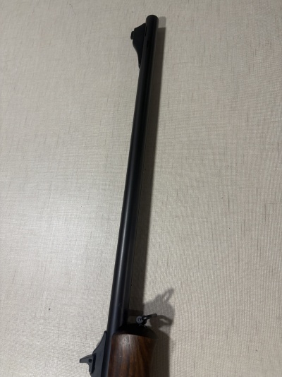 Arma de fogo com cano longo preto e cabo de madeira castanha sobre superfície branca.