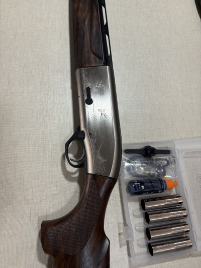 Espingarda com coronha de madeira e metal prateado com gravações, e acessórios num estojo plástico