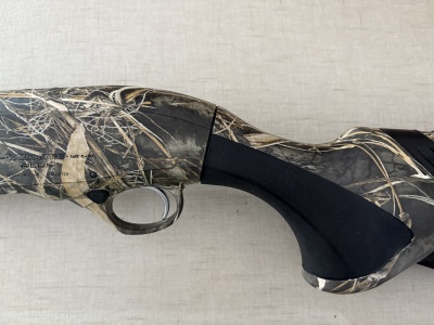 Parte de espingarda camuflada com padrão vegetação seca e punho preto em fundo bege