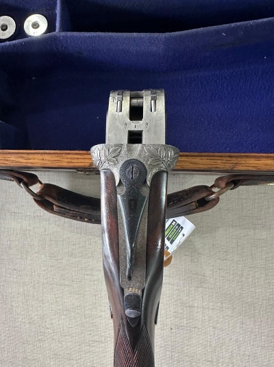 Espingarda com coronha de madeira e armação metálica prateada com detalhes florais na mala azul