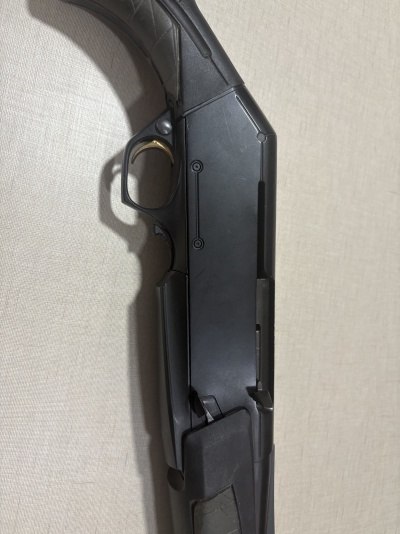 Parte de arma de fogo preta com gatilho dourado em superfície bege.