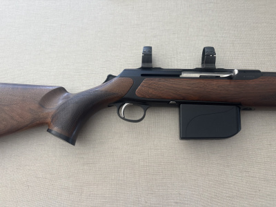 Rifle com coronha em madeira castanha e arma metálica preta sobre fundo bege texturizado.