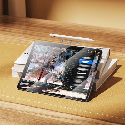 Tablet cinza escuro com aplicação de pintura digital, sobre livros em superfície de madeira e base de couro com caneta flutuante.