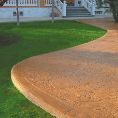 Pavimento em betão estampado castanho claro junto a relva verde e escadaria em pedra branca.