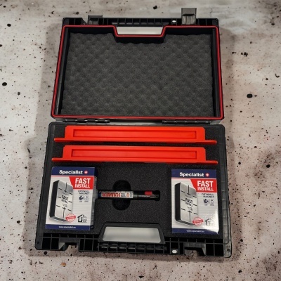 Mala preta com material de espuma, duas caixas Specialist FAST INSTALL, duas peças vermelhas e marcador, sobre mesa cinzenta