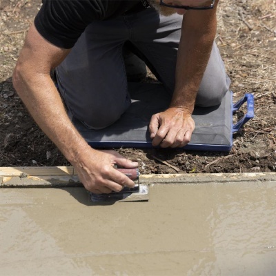 Pessoa a alisar cimento com desempenadeira, ajoelhada num almofadão azul