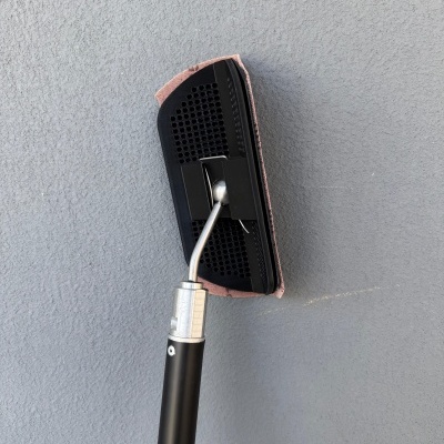 Esfregona com cabo preto e cabeça preta com pano cor de rosa contra parede cinzenta.