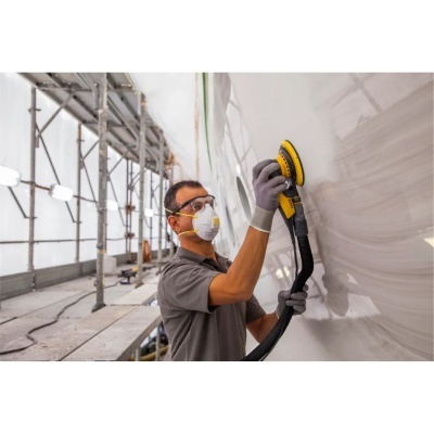 Homem a lixar parede com lixadora numa obra com andaimes