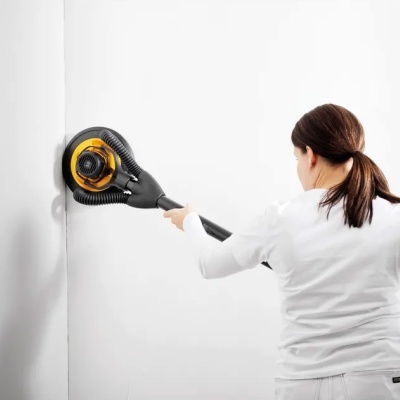 Mulher usando martelo perfurador elétrico amarelo e preto para lixar parede branca