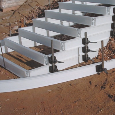 Estrutura branca de escada metálica apoiada em solo de terra com fixadores.