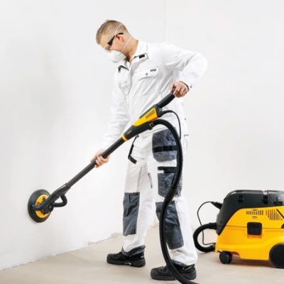 Homem a usar lixadora elétrica amarela e preta em parede branca