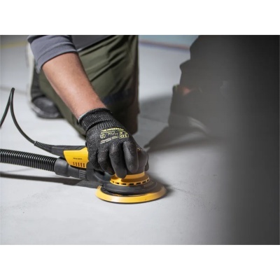 Amoladora elétrica amarela e preta com mão de luva a usá-la numa superfície cinzenta.