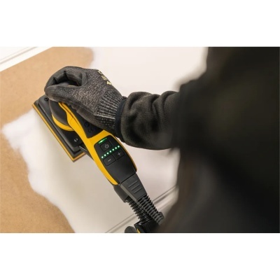 Lixadeira elétrica amarela e preta em uso com luva preta em superfície de madeira clara