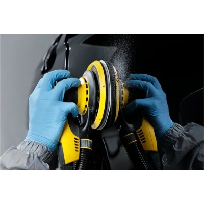Máquina de polir amarela e preta usada com luvas azuis sobre superfície preta