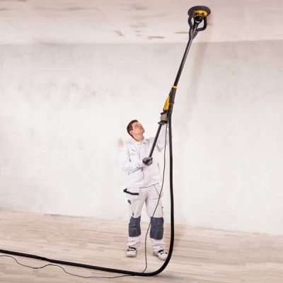 Homem a usar lixadora elétrica de parede com cabo longo para alisar teto