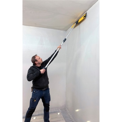 Homem a limpar ou pintar tecto branco com ferramenta de cabo longo num interior