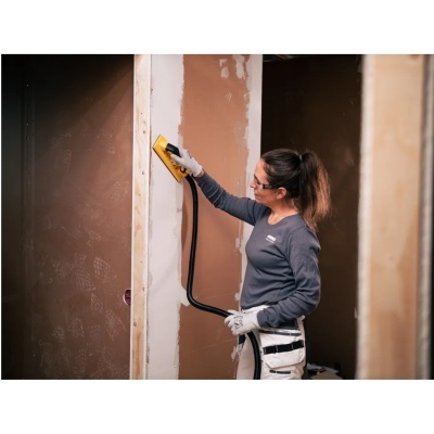 Mulher a lixar parede interior com ferramenta amarela