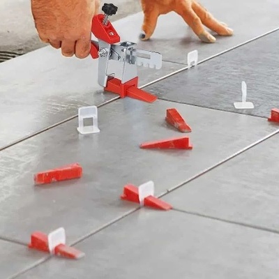 Pessoa a usar ferramenta de nivelamento em azulejos cinzentos com espaçadores vermelhos e brancos