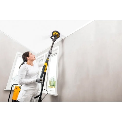 Mulher a usar lixadora elétrica amarela e preta em parede interior cinzenta