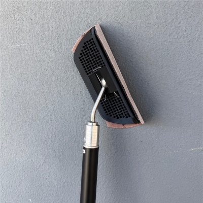 Esfregona preta com cabo e superfície de contacto rosa encostada a uma parede cinza