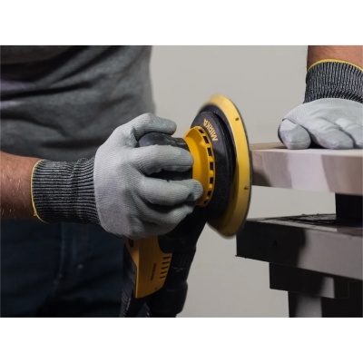 Lixadora elétrica amarela e preta a ser usada para lixar uma superfície clara numa mesa escura.