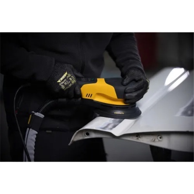 Lixadora elétrica amarela e preta a polir superfície branca com luvas pretas