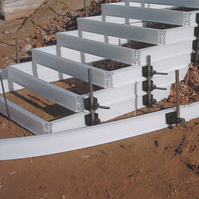 Estrutura branca de escada metálica apoiada em solo de terra com fixadores.
