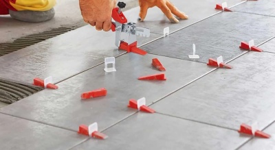 Pessoa a usar ferramenta de nivelamento em azulejos cinzentos com espaçadores vermelhos e brancos