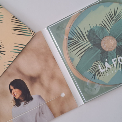 CD com design de folhas verdes, texto LISBÔA, invólucro bege com padrão de folhas e livreto com foto de mulher