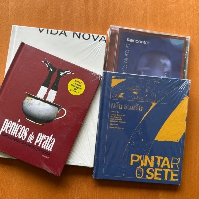 Livros e CD embalados em plástico sobre mesa de madeira.