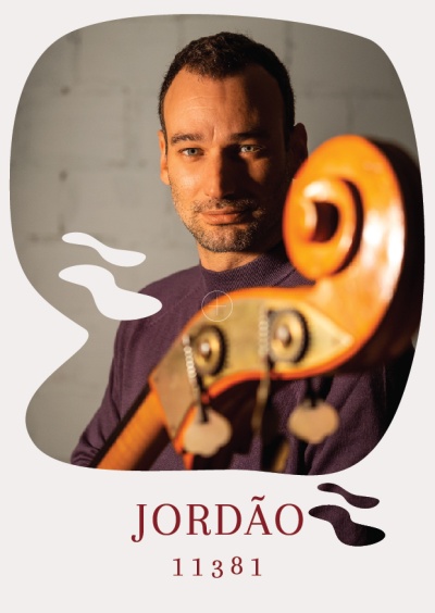 Homem com camisola roxa segurando um violoncelo de madeira clara com texto JORDÃO 11381