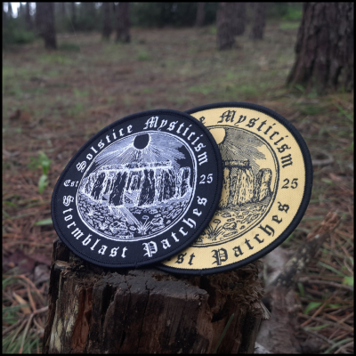 Duas patches redondas com ilustração do Stonehenge, uma preta e outra bege num cepo de árvore