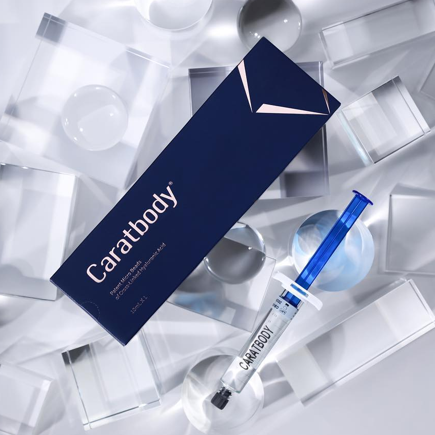 Embalagem azul e seringa do Caratbody sobre superfície com formas geométricas transparentes