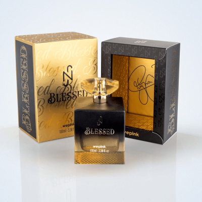 Frasco de perfume preto e dourado com duas embalagens ao fundo